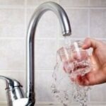 Hand holding a clear glass under a chrome-finished faucet, filling with fresh water from B&L Plumbing services.