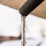 Dripping water from a pipe with icicles in a cold winter setting, highlighting frozen pipe risks. B&L Plumbing services help.