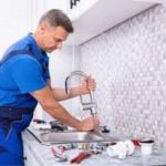 Plumber working on a kitchen sink faucet with plumbing tools in a modern Colorado Springs home.