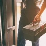 Individual in casual attire holding a toolbox by an open doorway, illustrating plumbing maintenance by B&L Plumbing.