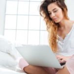Young woman in casual attire using a laptop on a bed, promoting reliable plumbing service from B&L Plumbing.