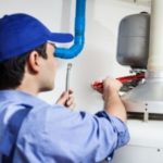Plumber in blue cap repairing a water heater with a plumbing wrench at B&L Plumbing service.