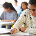 Female student studying in a classroom with a notebook, pencil, and laptop, promoting learning about water heaters.