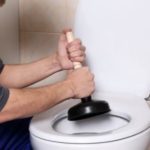 Person using a plunger to clear a toilet in a bathroom, highlighting essential plumbing maintenance by B&L Plumbing.