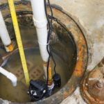 Sump pump installation with water in sump pit and pipes, showcasing B&L Plumbing's services for homeowners.