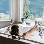 Individual relaxing in a modern bathtub with a scenic window view, featuring wine and towels, by B&L Plumbing.