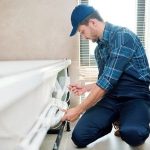 Technician repairing a washing machine with plumbing tools for B&L Plumbing bathroom remodeling services.