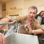 A man repairing a kitchen sink with tools while a woman talks on the phone, representing B&L Plumbing services.