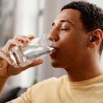 Young man savoring a glass of water in a bright setting, promoting home hydration and filtration by B&L Plumbing.