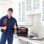 Smiling handyman with a wrench in a bright kitchen, ready to assist B&L Plumbing customers with water hammer solutions.
