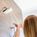Person showering in modern bathroom; sleek showerhead with gentle water spray, highlighting water heater upgrade benefits.