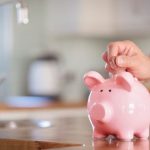 Person's hand adding money to a pink piggy bank, illustrating water conservation and savings with B&L Plumbing's tips.