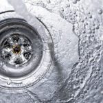 Metal sink drain with cascading water, illustrating B&L Plumbing's tips for preventing sewer line clogs.