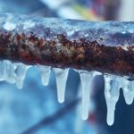 Icy pipe with icicles and rust, highlighting winter conditions and plumbing issues for B&L Plumbing services.