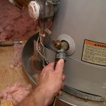 A hand adjusting a valve on a water heater, highlighting maintenance for faulty plumbing systems.
