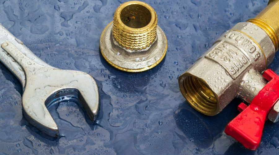 Wrench, brass fitting, and valve on wet surface, representing plumbing tools and components relevant to plumbing services and repairs.
