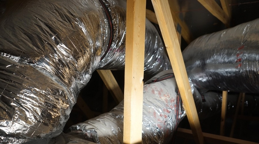Ductwork in an attic space, showcasing insulated metal ducts and wooden framing, relevant to air duct maintenance and HVAC efficiency.