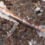 Damaged copper pipe with ice and debris, illustrating the risks of frozen pipes during winter plumbing emergencies.