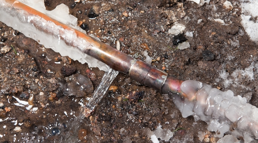 Frozen copper pipe with ice and water leakage, illustrating plumbing issues during winter, relevant to preventing frozen pipes and plumbing protection tips.